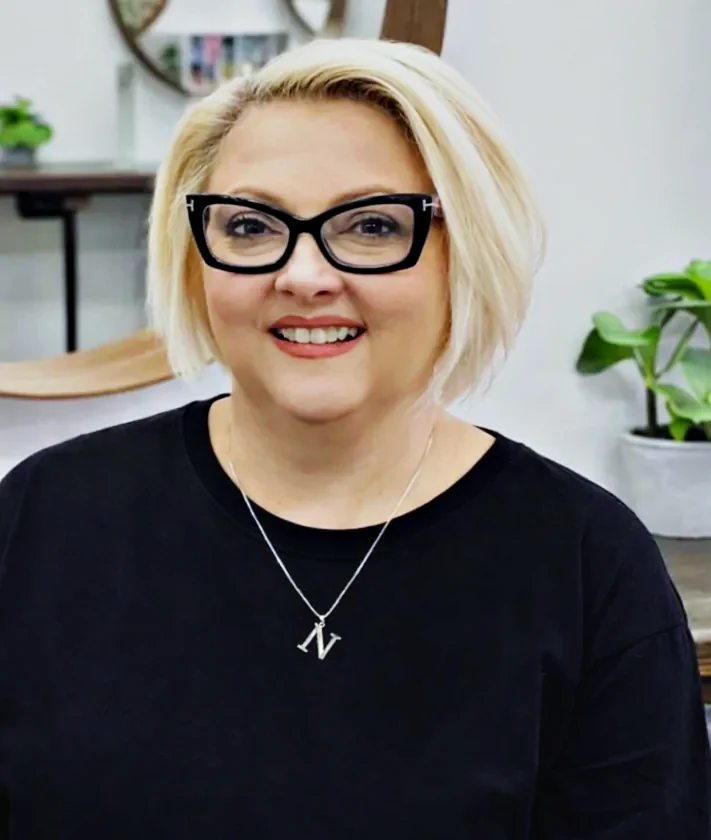 Nicole, Master Stylist at Hair Management Co in Gymea, smiling in the salon with a blonde bob and black glasses