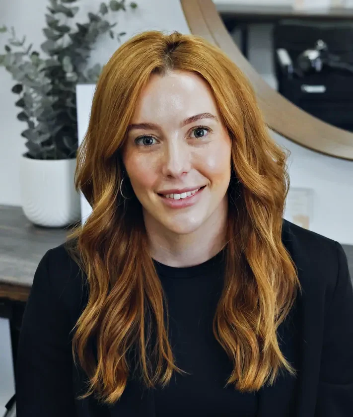 Courtney, Master Stylist at Hair Management Co in Gymea, smiling in the salon with long copper waves