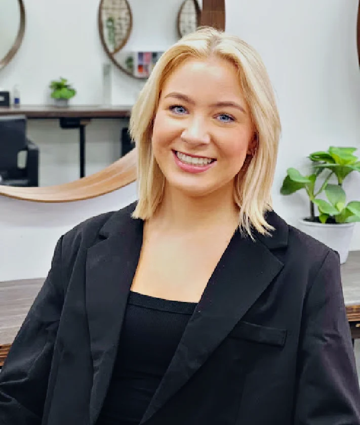 Tayla, Senior Stylist at Hair Management Co in Gymea, smiling in the salon with a blonde bob and a black blazer