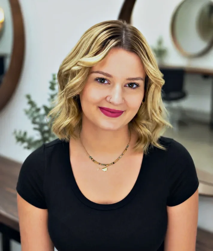 Tiela, Emerging Senior Stylist at Hair Management Co in Gymea, smiling in the salon with wavy blonde shoulder-length hair