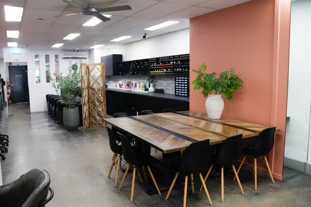 Timber communal table and terracotta feature wall at Hair Management Co, an inclusive hair salon in Gymea